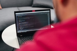 Over-the-shoulder view of a person working on a laptop displaying lines of programming code, representing software development and source system management.