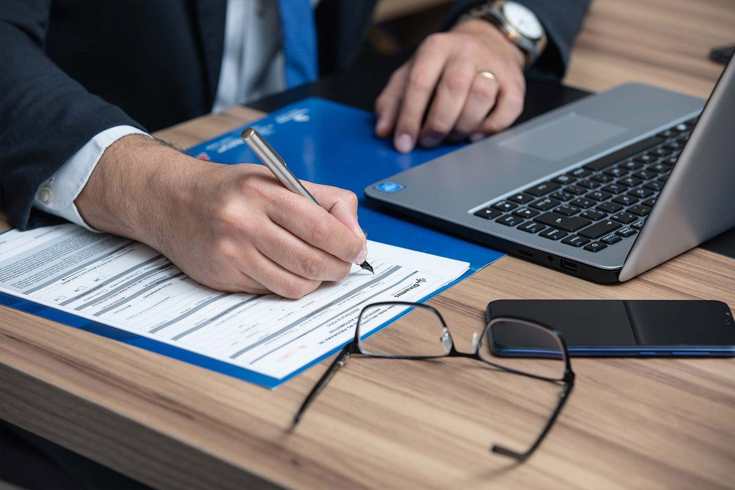 A man filling a paper form next to a laptop