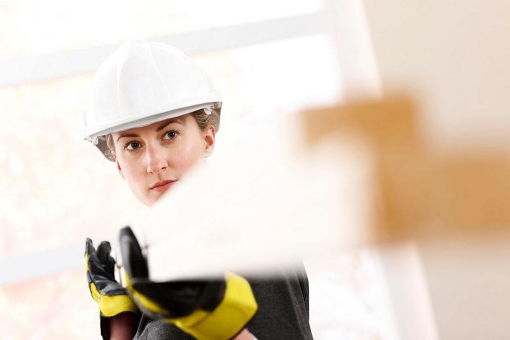 A helmeted builder holding two planks in her hands