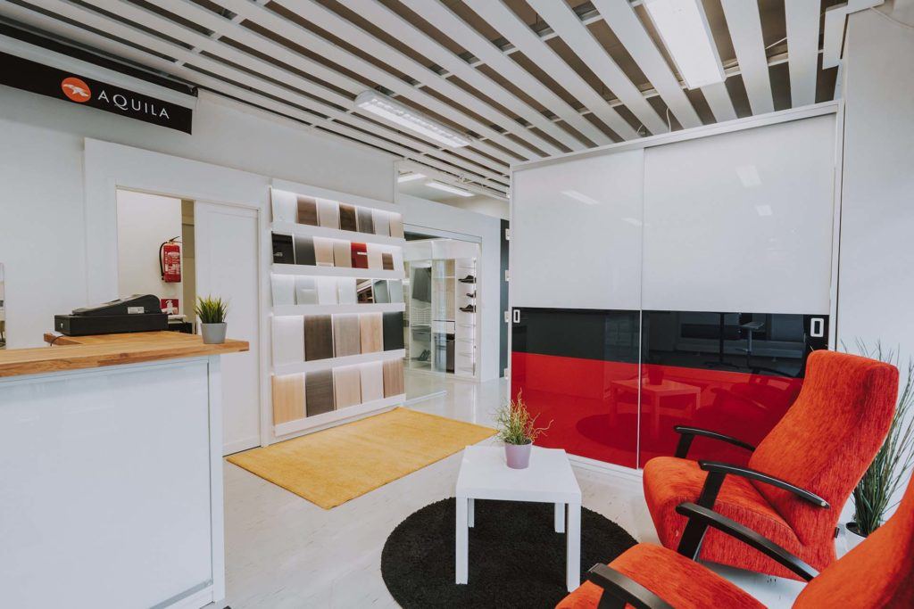 Trendi Kaihtimen toimiston vastaanottotiski, näytteitä materiaaleista seinällä ja kaksi punaista nojatuolia