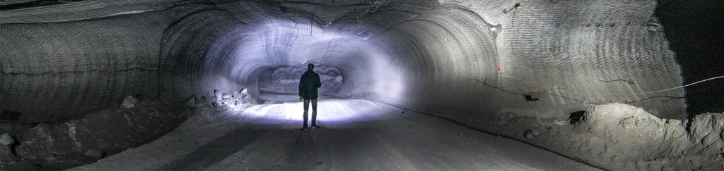 Mies osoittaa taskulampulla kaivostunnelin syvyyksiin