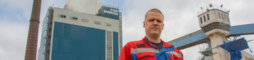An employee of Pori Energia standing before a power plant holding a handful of chips
